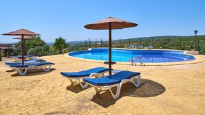 Ein Poolbereich mit Liegestühlen und Sonnenschirmen, umgeben von einer gefliesten Terrasse.