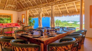 A dining area with a thatched roof, wooden table, and chairs. - Casa Torre Del Cielo / Ocean Views, Pool & Privacy (Careyes)