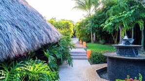 A pathway leading to a thatched-roof structure surrounded by lush greenery and a small fountain. - Casa Torre Del Cielo / Ocean Views, Pool & Privacy (Careyes)