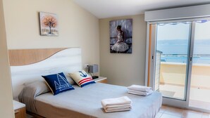 A bedroom with a bed, a nightstand, a painting, and a view of the sea.