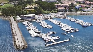 An aerial view of a marina with numerous boats docked, a pier, and buildings in the background.