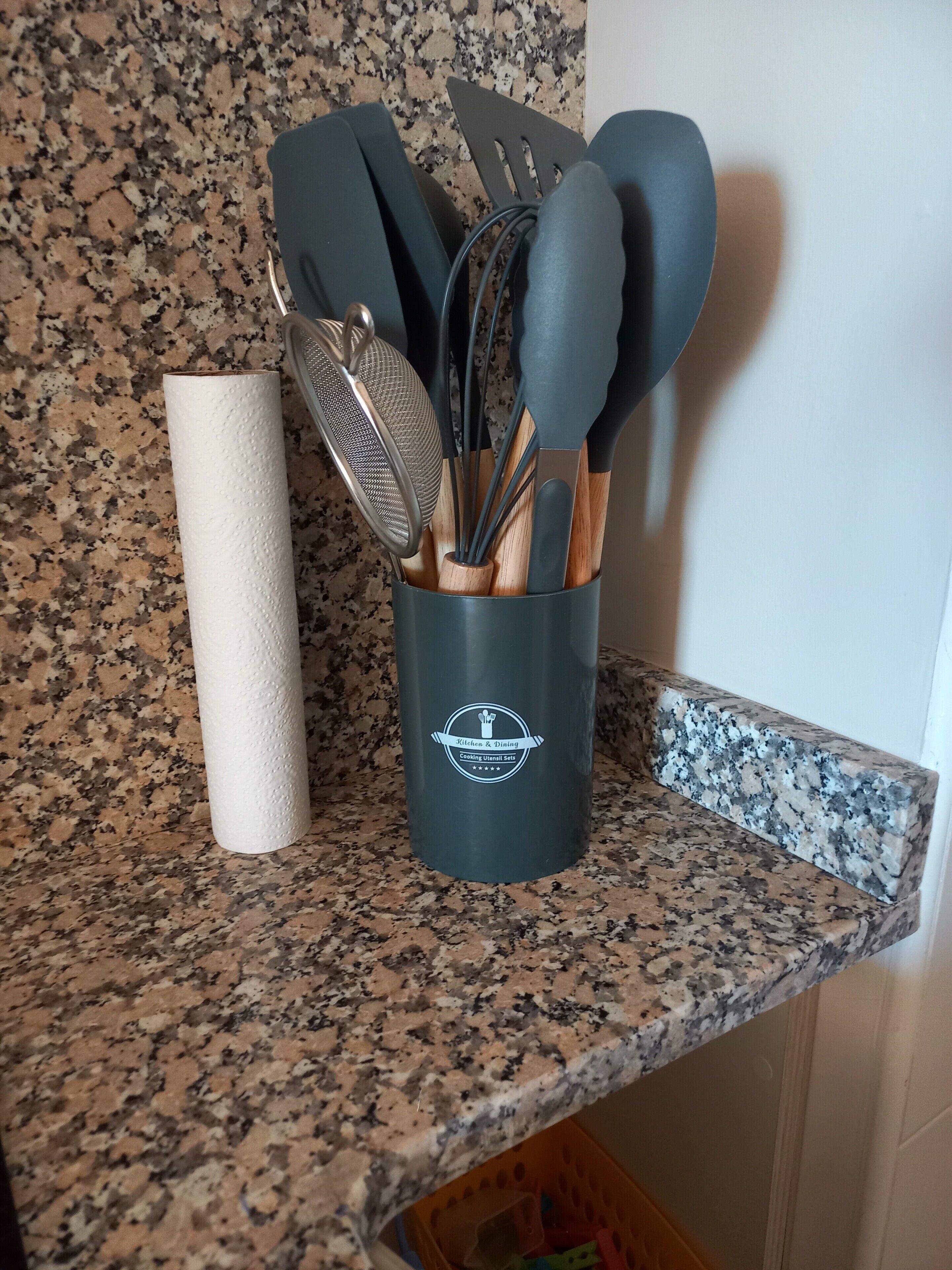 Un porte-ustensiles de cuisine avec un rouleau d’essuie-tout posé sur un comptoir en granit.
