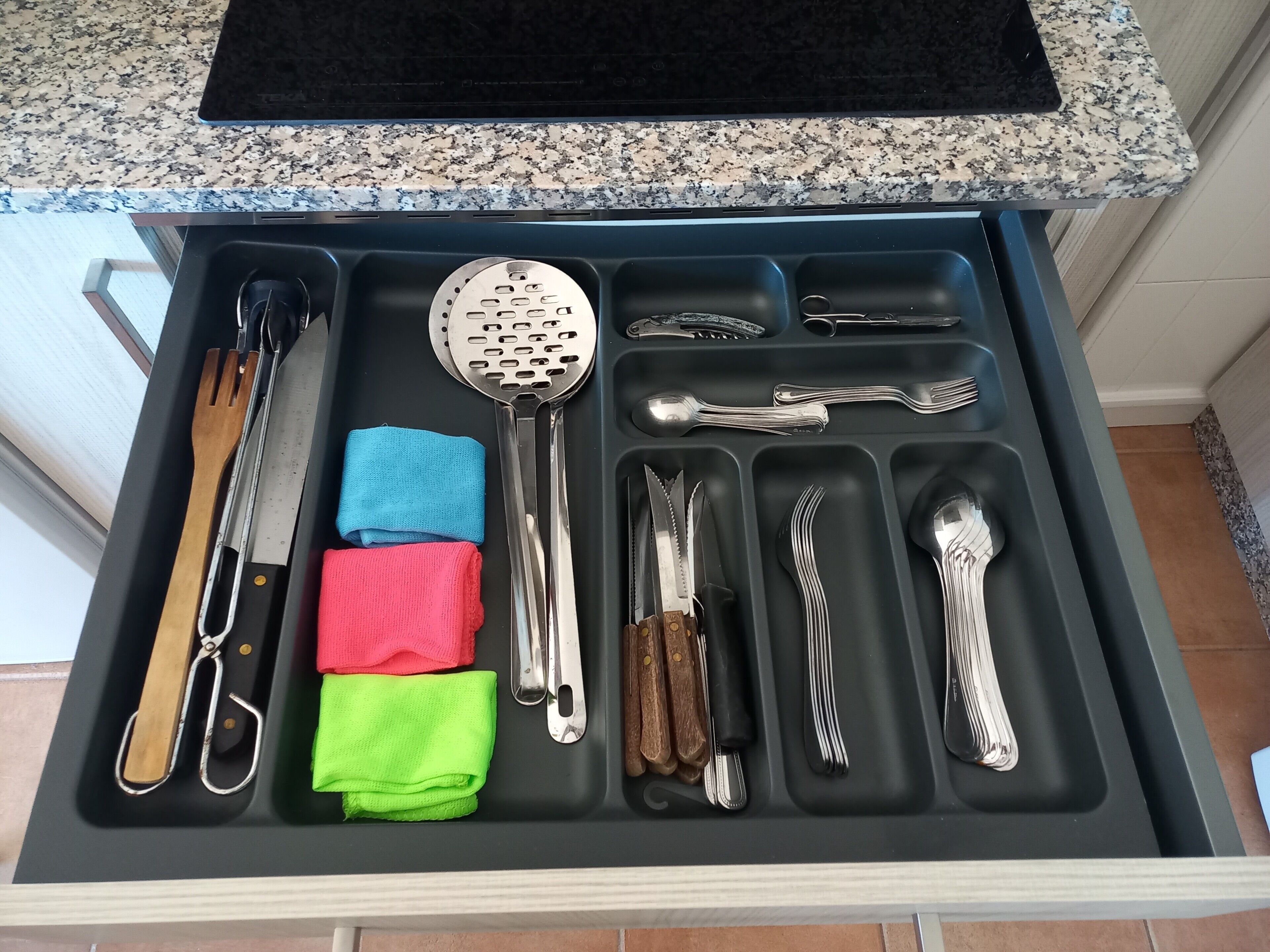 A kitchen drawer with utensils and cloths.