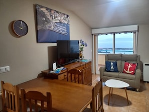 A living room with a dining table, TV, and a sofa with nautical-themed pillows.