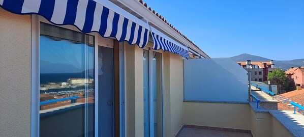 A building with a blue and white striped awning, large glass sliding doors, and a view of the sea.