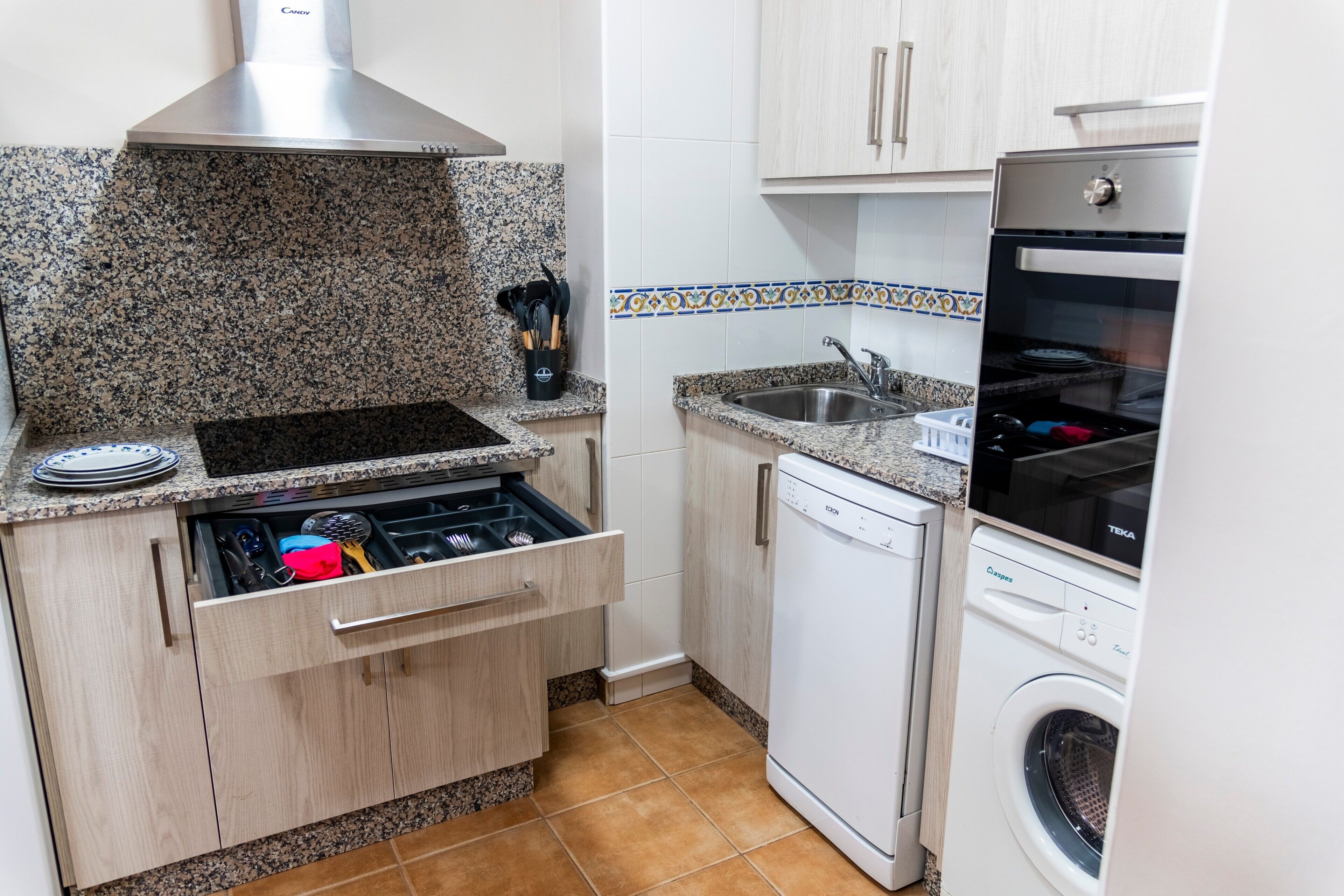 Une cuisine compacte dotée de plans de travail en granit, d’une cuisinière encastrée, d’un lave-vaisselle et d’une machine à laver.