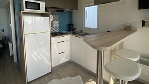 A compact kitchen with a microwave, stove, and sink. There are two stools and a small rug.