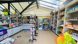 A pharmacy with shelves stocked with various products, a display of promotional items, and a counter with a newspaper.