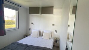 A modern hotel room with a large bed, two bedside tables, a window with curtains, and a mirror.