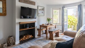 Ein gemütliches Wohnzimmer mit Kamin, Fernseher, Esstisch und Blick ins Freie.
