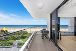 A balcony with a view of the beach, a lifeguard station, and a table with chairs. - Absolute Beachfront Beauty (Gold Coast)