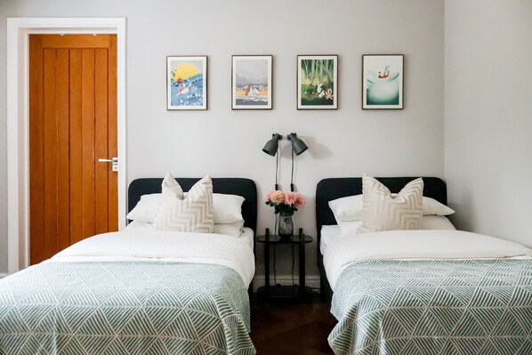 A room with two beds, a wooden door, and four framed pictures on the wall.