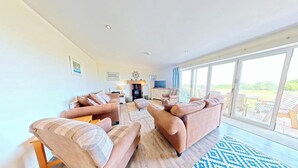 A spacious living room with a fireplace, comfortable seating, and a large sliding glass door leading to an outdoor area. - Len's Lookout -  a cottage that sleeps 8 guests  in 4 bedrooms (Filey)