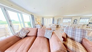 A spacious living area with a large sofa set, a dining table with chairs, and a kitchen area. - Len's Lookout -  a cottage that sleeps 8 guests  in 4 bedrooms (Filey)