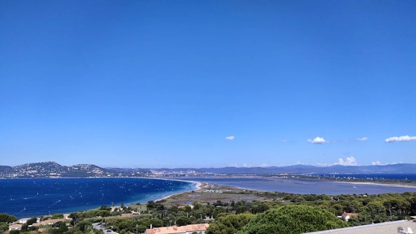Un paisaje costero con cielo despejado, una playa y una cadena montañosa distante.