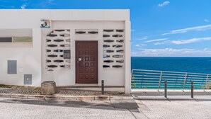 A building with a brown door, a white facade, and a view of the sea. - Apartment 'Oásis' with Sea View, Wi-Fi and Air Conditioning (Sesimbra)