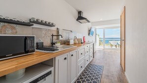 A modern kitchen with a microwave, toaster, and coffee maker, a wooden countertop, and a view to the outside. - Apartment 'Oásis' with Sea View, Wi-Fi and Air Conditioning (Sesimbra)
