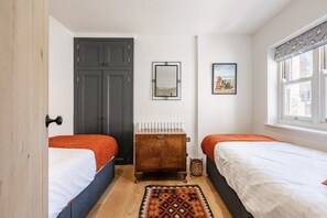A bedroom with two beds, a dresser, a mirror, a radiator, and a window with a view.