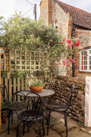 A stone building with a tiled roof, a wooden fence, and a table with chairs in front.