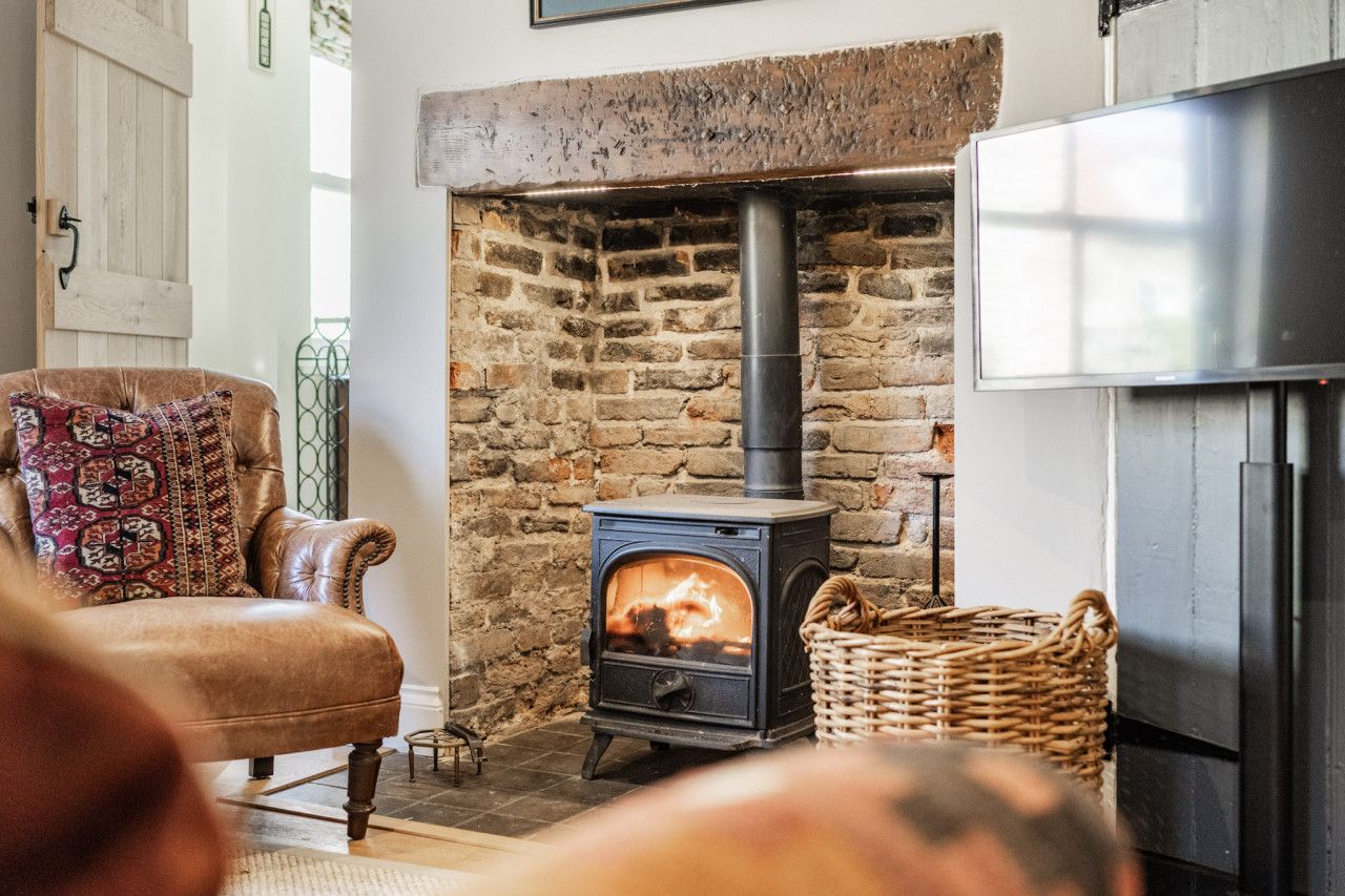 A cozy room with a stone fireplace, a leather armchair, and a modern refrigerator.