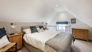 Une chambre à coucher comprenant un lit, des tables de chevet, une chaise, une commode et une fenêtre donnant sur un paysage agréable.