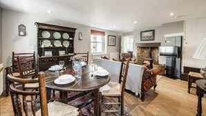 Un coin repas avec une table ronde en bois, dressée pour quatre personnes, entourée de chaises rembourrées. Un buffet intégré, doté de plusieurs étagères, est visible sur la gauche.