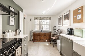 A compact kitchen with a stove, oven, and a coffee machine. There is a window with a view of buildings outside, and a corkboard with notes on the wall.