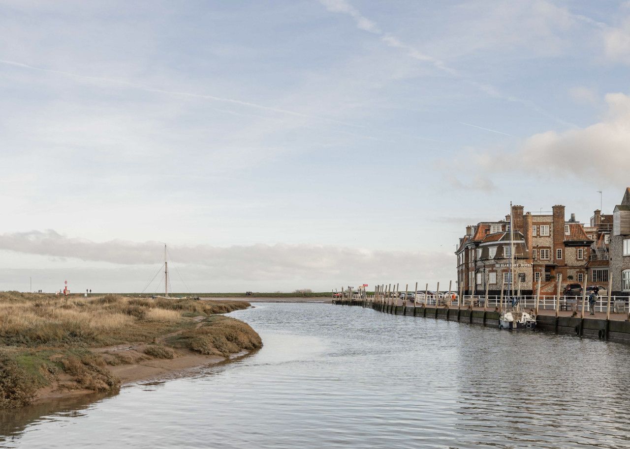 A riverside hotel with a dock extending into the water, a grassy bank, and a clear sky.