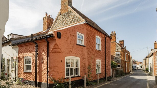 Une maison traditionnelle en briques rouges, avec des encadrements de fenêtres blancs, un toit à deux versants et une cheminée bien visible.