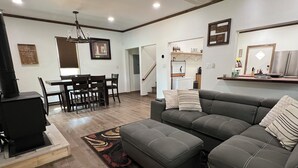 A modern living room with a gray sectional sofa, a dining table with chairs, a ceiling fan, and a patterned rug. - Charming 3-BR Cabin/House, Pool, creek, 35Acres with Fiber Internet in Pikeville (Pikeville)