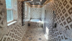 A modern bathroom with a stone-tiled floor, a built-in bathtub, and a shower area. - Charming 3-BR Cabin/House, Pool, creek, 35Acres with Fiber Internet in Pikeville (Pikeville)