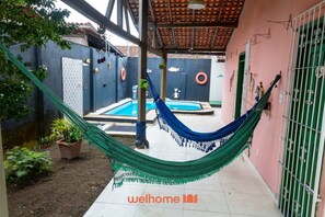 A hammock in a covered outdoor area with a pool and a tiled floor. - Casa na Ilha com Churrasqueira (Mosqueiro)