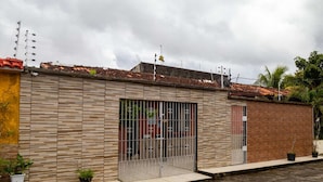 A modern building with a tiled roof, a large window with metal bars, and a brick wall. - Casa na Ilha com Churrasqueira (Mosqueiro)
