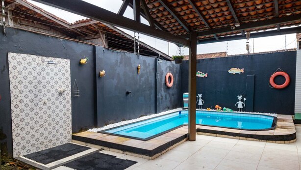 A swimming pool with a tiled deck, a covered area with a tiled roof, and a wall with decorative tiles and life rings. - Casa na Ilha com Churrasqueira (Mosqueiro)