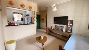 A living room with a TV mounted on the wall, a wooden bench, and a small table. - Casa na Ilha com Churrasqueira (Mosqueiro)