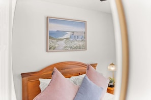 Quarto com cabeceira de madeira, quadro emoldurado com paisagem costeira e luminária de cabeceira.