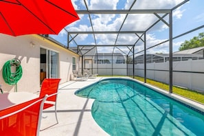 Uma piscina com cobertura de vidro, cadeiras e guarda-sol vermelhos.