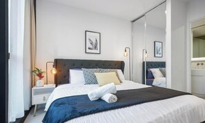 Quarto com cama, mesas de cabeceira, espelho e quadros na parede.