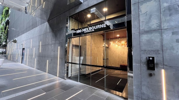 A modern building facade with a glass entrance, a sign reading "380 MELBOURNE," and a visible parcel delivery service.