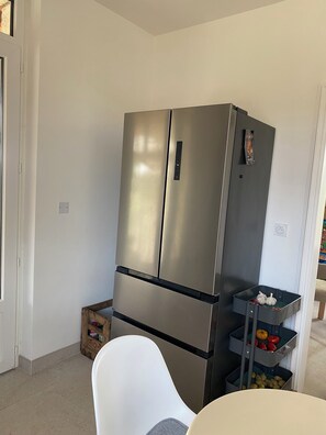 A compact kitchen with a stainless steel refrigerator, a white chair, and a small wooden crate.