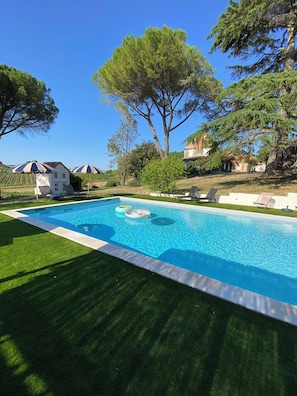 A swimming pool with a clear blue water, surrounded by a well-maintained lawn and trees.