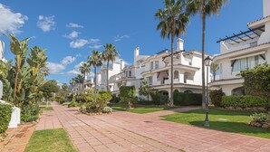 A residential area with white buildings, palm trees, and a paved walkway.
