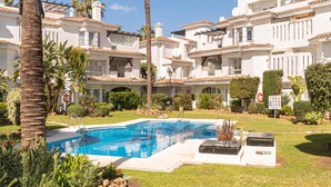 A pool area with a clear blue pool, surrounded by palm trees and a white building with multiple balconies.