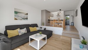 A modern living room with a sofa, coffee table, and a painting of a beach scene.