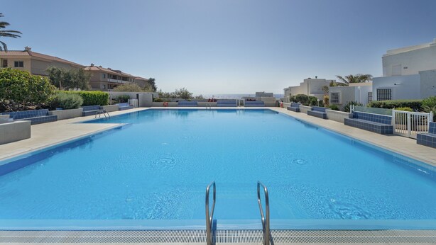 A rectangular swimming pool with a clear blue surface, surrounded by a low wall and a metal ladder.