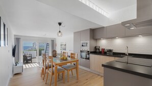 A modern kitchen with a dining area, wooden flooring, and a view through the glass door.