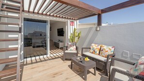 A modern outdoor patio with wicker furniture, a glass door leading to an interior space, and a clear view of the sky.