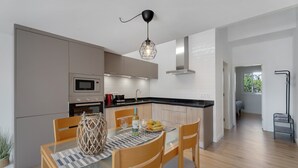 A modern kitchen with a dining area, featuring a glass table, wooden chairs, a woven basket, and a pendant light.