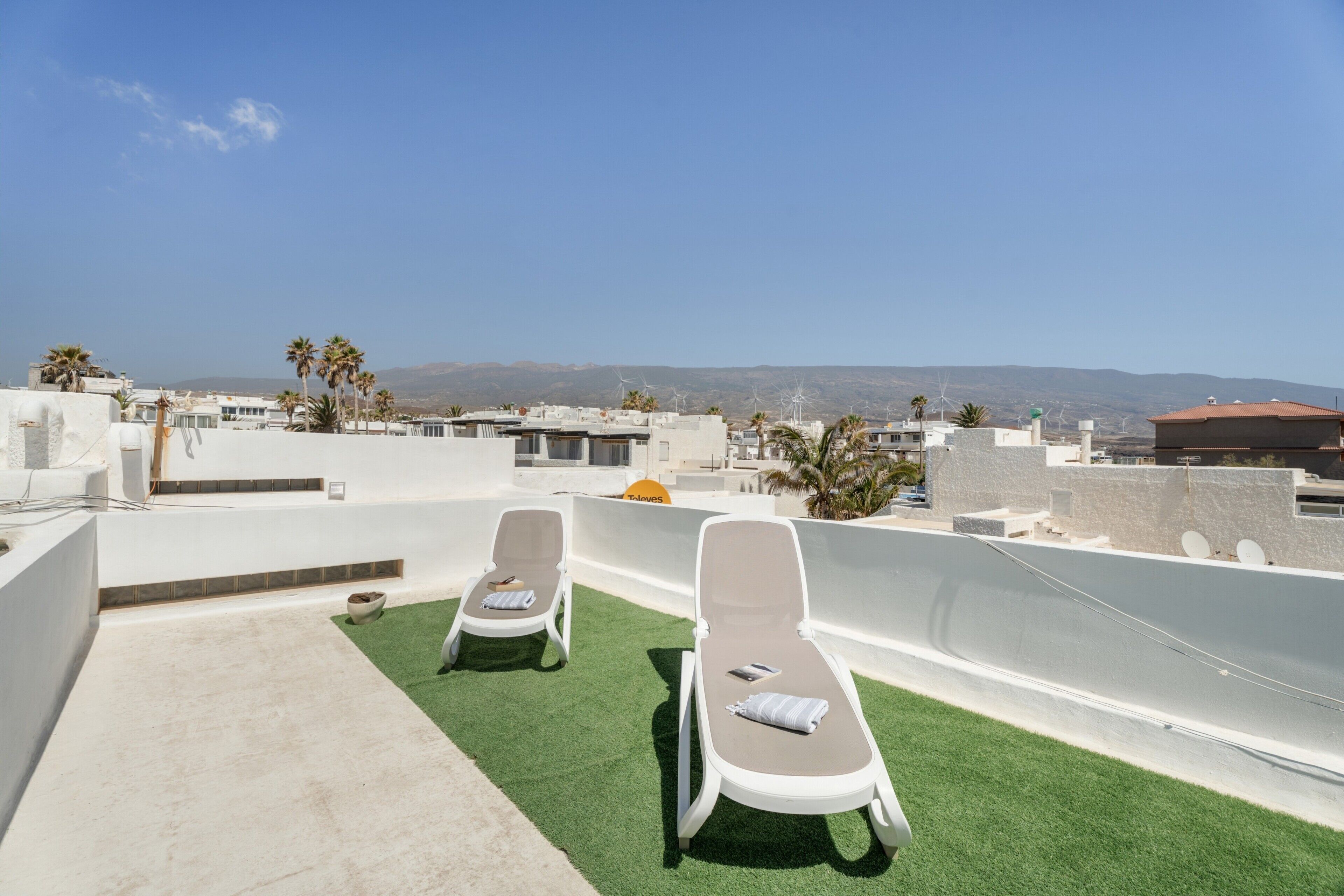 A rooftop terrace with two sun loungers, artificial grass, and a clear view of the cityscape and mountains.
