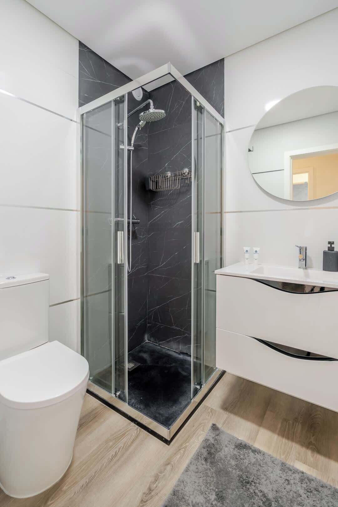 Une salle de bain moderne avec une douche à parois de verre, des toilettes blanches et un meuble-lavabo avec un miroir.